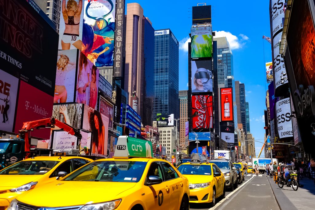Times Square with yellow New York City Taxi cabs and tour buses driving through colorful billboards. Manhattan, New York. USA - August 25, 2015.