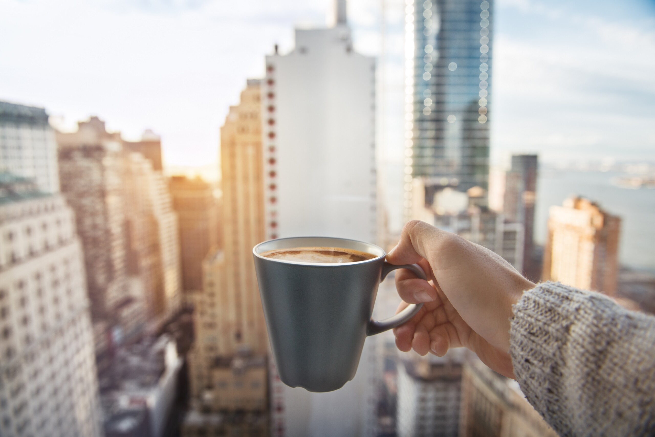 Mężczyzna trzymający filiżankę kawy w luksusowych apartamentach z widokiem na centrum Manhattanu.
